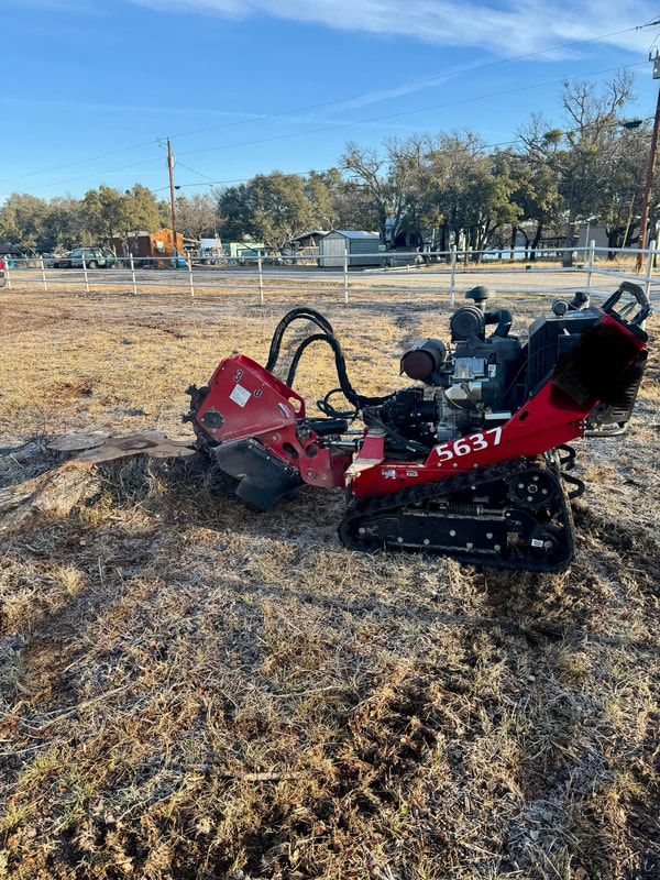 Red tracked stump grinder positioned next to a ground-down stump in an open pasture with a white fence line behind